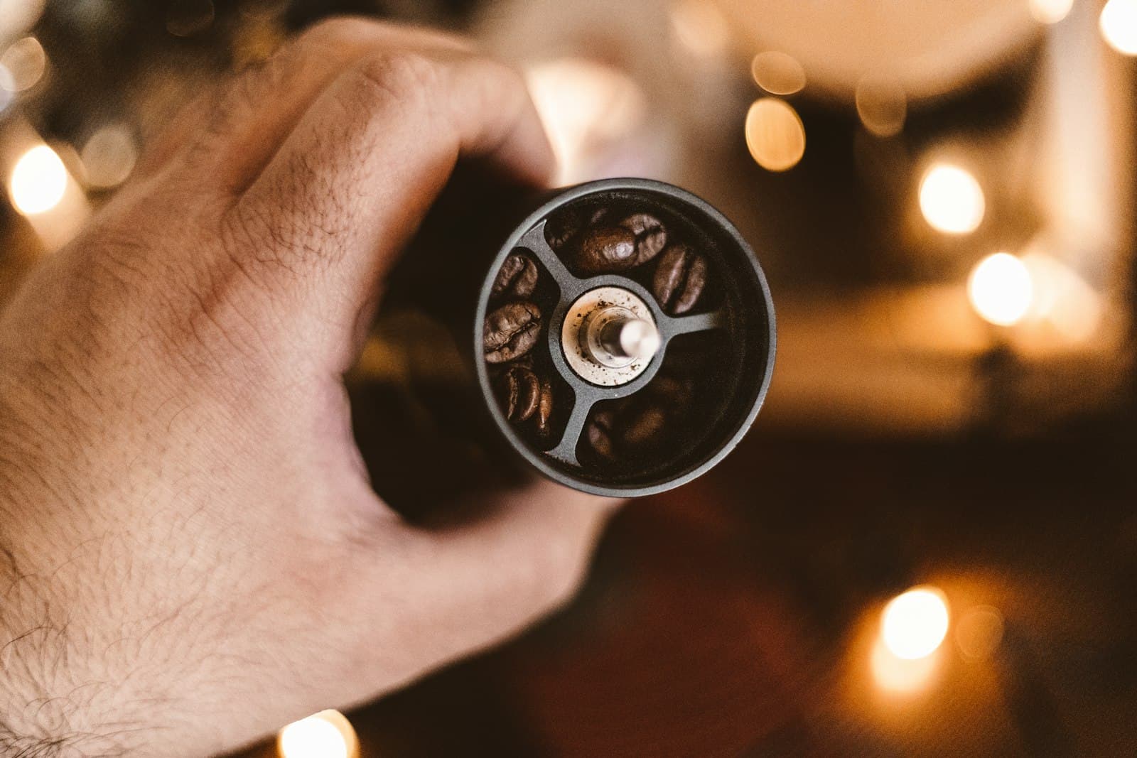 A hand holding a manual coffee grinder filled with beans