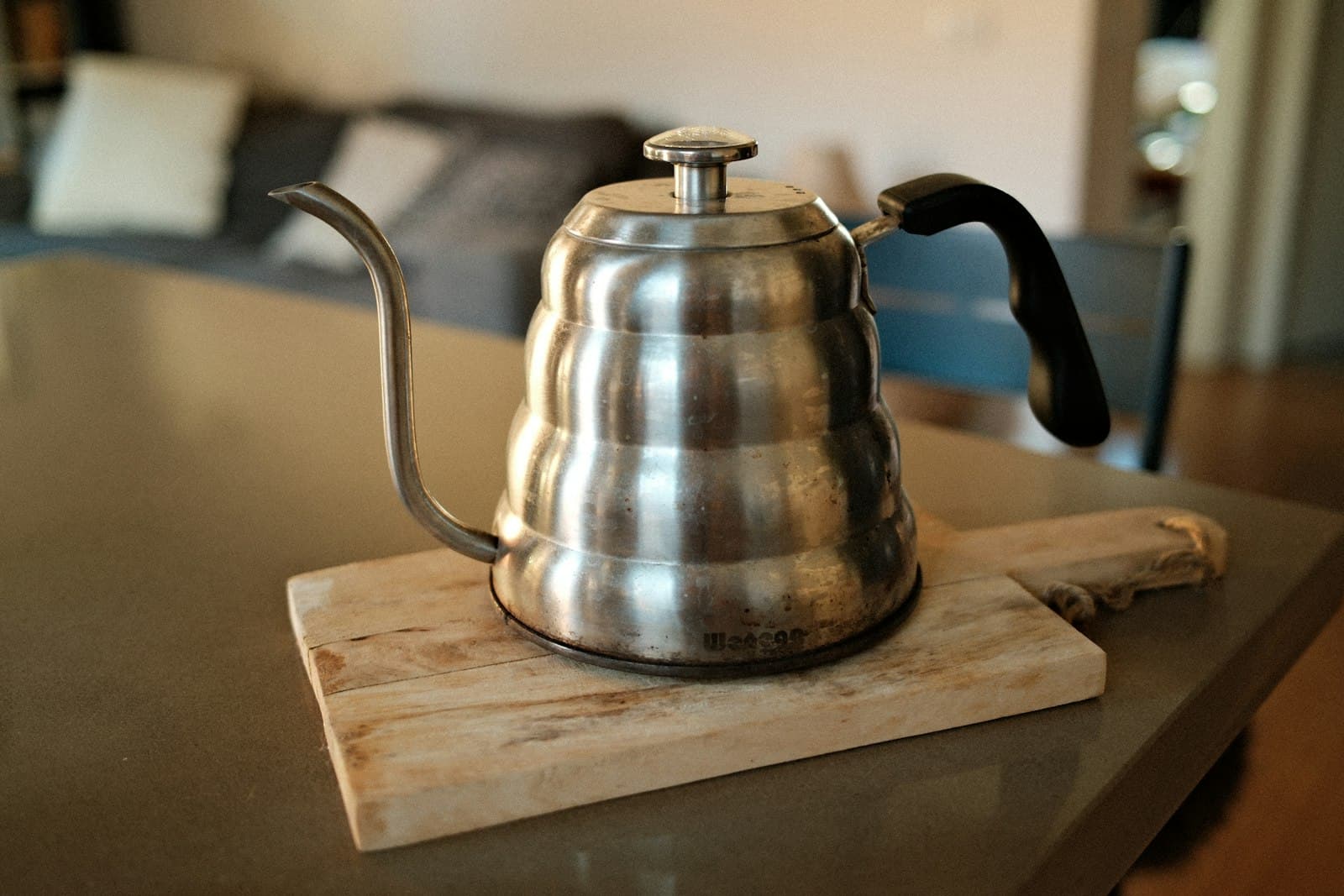 A stainless gooseneck kettle on a wooden board
