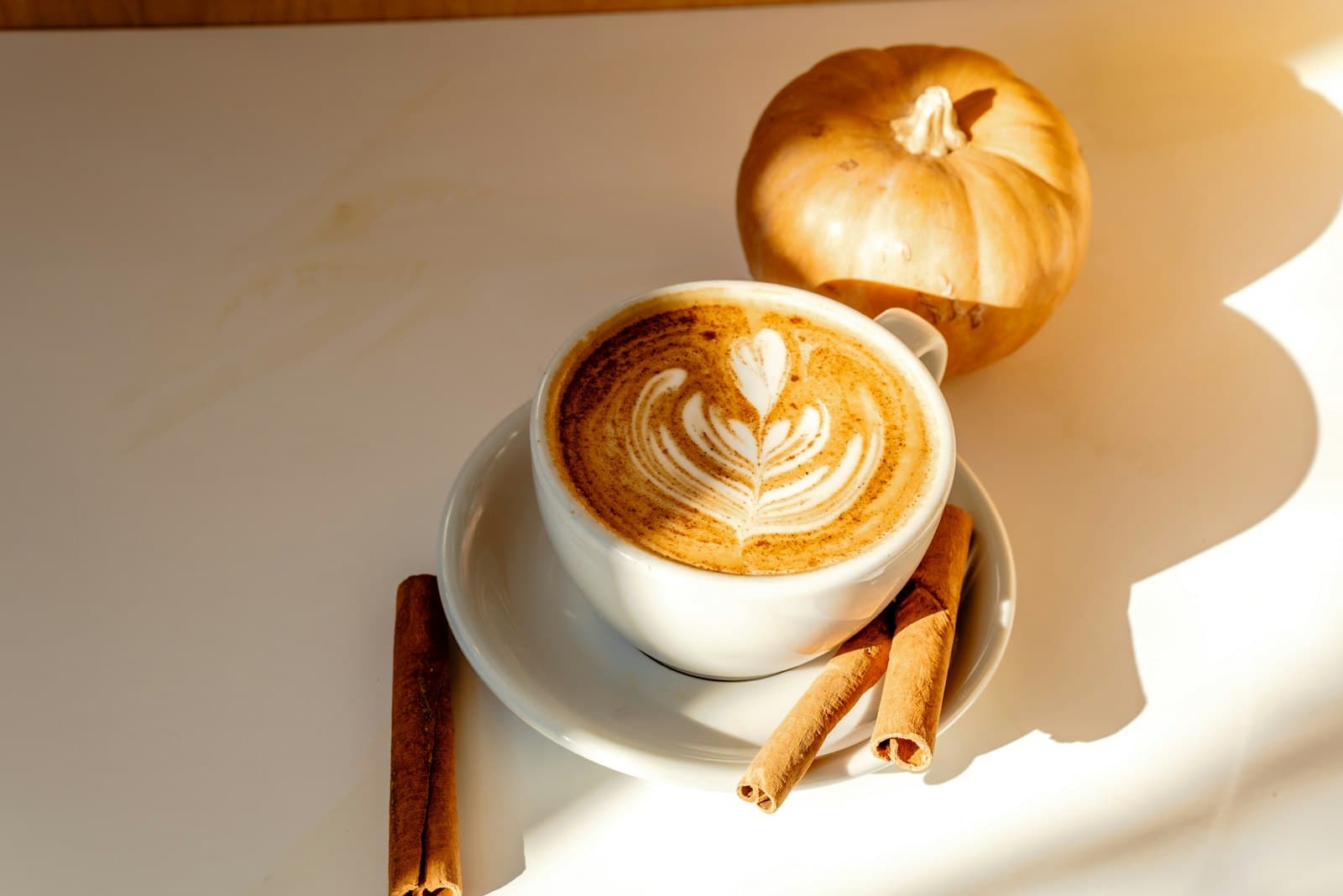 A frothy cappuccino with cinnamon sticks on the table