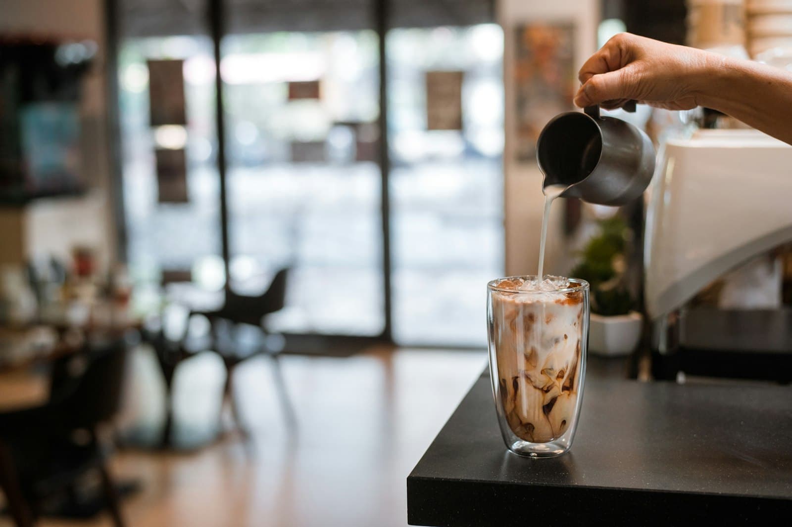 Milk pouring into a tall glass of iced coffee in layers